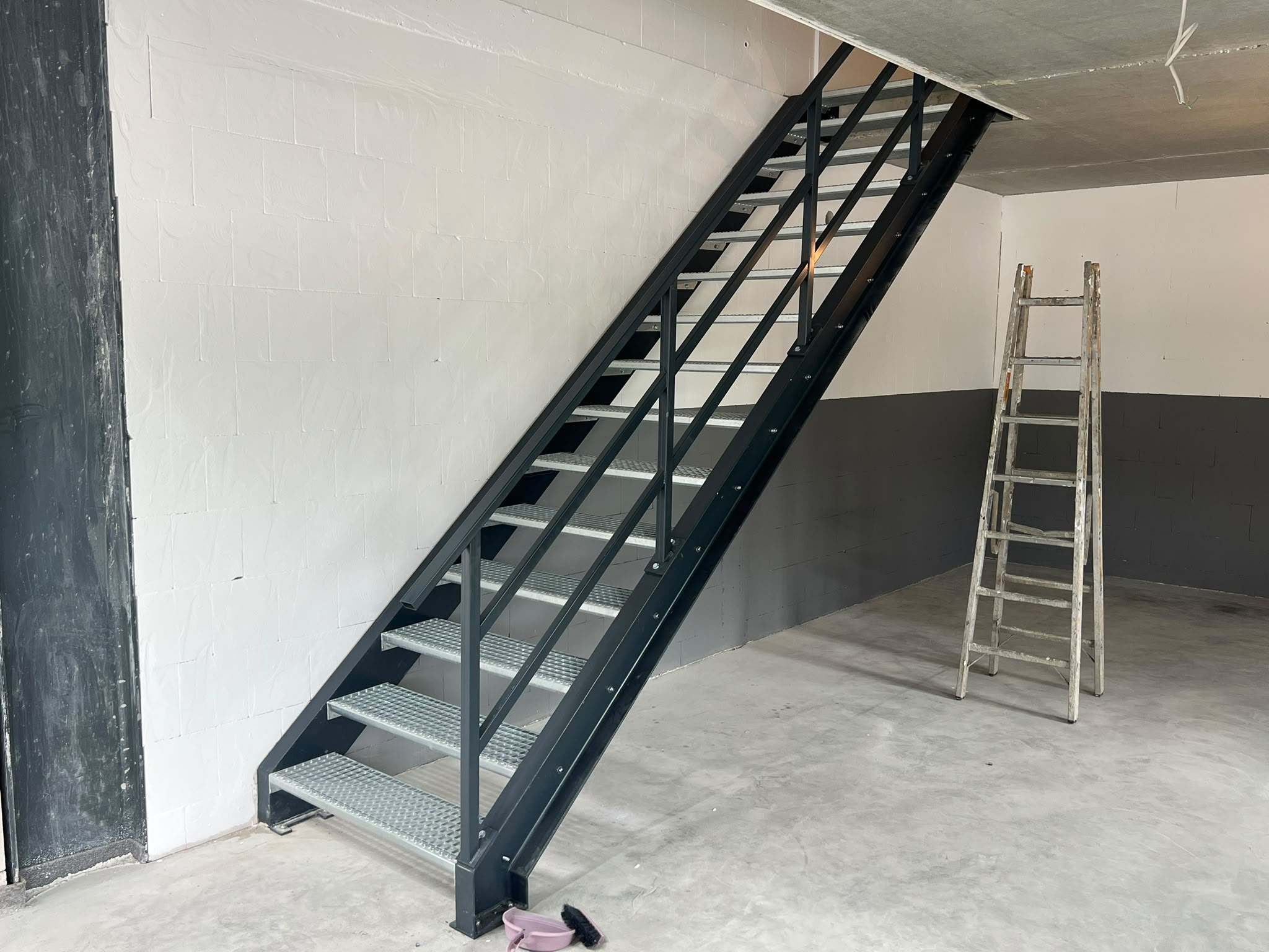 Gerade anthrazitfarbene Stahltreppe mit verzinkten Gitterroststufen und Geländer mit zwei Knieleisten in einer Werkstatt